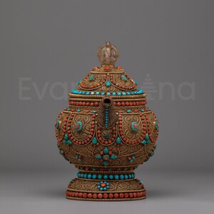 Peut inclure: Théière antique ornée avec des filigranes et des perles complexes. La théière présente une base en métal de couleur bronze, ornée de pierres turquoise et corail. Un bouton clair en forme de gemme surmonte le couvercle. Le design est détaillé et décoratif.