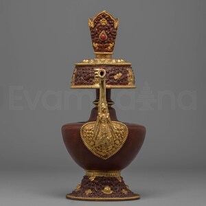 Peut inclure: Un récipient décoratif orné, marron et doré, avec des sculptures complexes et un accent de pierre précieuse rouge. Le récipient a une base bulbeuse, un long bec et un dessus décoratif. Le design est détaillé et présente des accents dorés.