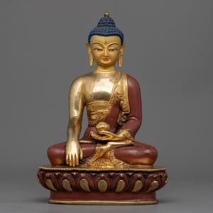 Peut inclure: Statue de Bouddha assis, corps doré et robe marron. La statue a une coiffe bleue et est assise sur une base de fleur de lotus. Elle tient un petit bol dans ses mains.