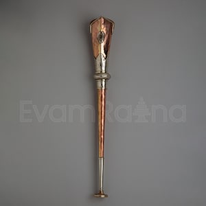 May include: A handcrafted copper and silver ceremonial staff with a decorative top. The staff features a copper body with silver accents and a gold-colored base. The top has a unique design with an oval opening.
