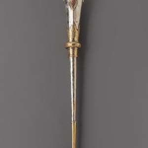 May include: A silver and gold ceremonial mace with a flared top. The top features a red gemstone and ornate gold detailing. The mace has a long, slender silver shaft and a gold base. The design is symmetrical and detailed.