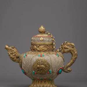 May include: Ornate gold and silver teapot with dragon-shaped spout and handle. The teapot features intricate patterns, turquoise and red accents, and a decorative lid with a chain. The base is gold, and the body is silver with embossed designs.