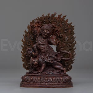 May include: A detailed, reddish-brown statue depicting a deity figure with multiple arms, a fierce expression, and a crown. The figure is riding a tiger and surrounded by a fiery halo. The statue is mounted on a decorative base.