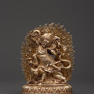 May include: A detailed silver statue of a deity with multiple arms, standing on a base with intricate designs. The figure is surrounded by a fiery halo and rides a feline. The statue is a representation of religious art.