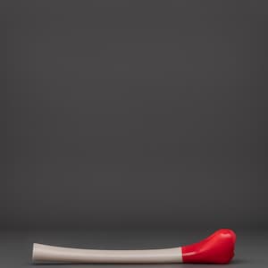May include: A curved, bone-colored object with a rounded, bright red end. The object is lying horizontally against a gray background. The design is simple and modern, with a smooth, glossy finish.
