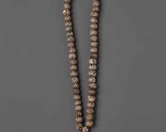 May include: A long strand of prayer beads with a red tassel. The beads are a light brown color with dark brown markings. The tassel is a deep red color. The beads are strung together with a white and red cord.