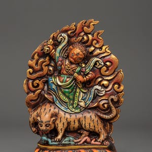May include: A detailed, hand-carved wooden statue depicting a figure riding a tiger, set against a backdrop of stylized flames. The statue features vibrant colors, including red, gold, and blue, and intricate details.
