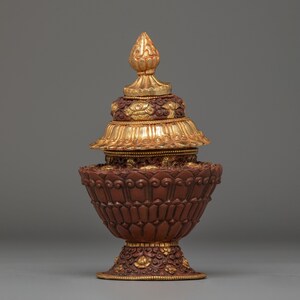 Peut inclure: Objet décoratif orné, de couleur or et marron. Il présente un design à plusieurs niveaux avec des motifs complexes et des accents floraux. Le sommet est une flèche dorée, et la base est en forme de bol marron. Il s'agit probablement d'un objet religieux ou cérémoniel.