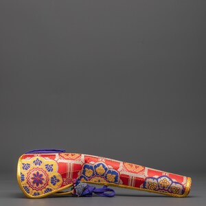 May include: A decorative, elongated case with a red background and intricate floral patterns in gold and blue. The case has a gold trim and a blue accent at the end. The design is symmetrical and detailed.