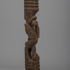 May include: A carved wooden sculpture with a weathered, brown finish. The sculpture features a stylized human figure with intricate details, including a headdress and carved facial features. The piece is approximately 18 inches tall.