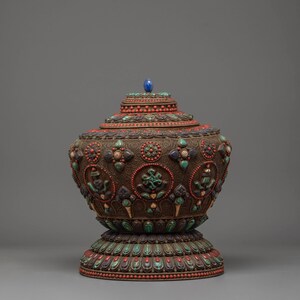 Peut inclure: Vase décoratif de style antique orné, avec un couvercle. Le vase marron présente des motifs complexes et est orné d'accents rouges, turquoise et bleus. Un joyau bleu surmonte le couvercle. La base est également décorée de couleurs similaires.