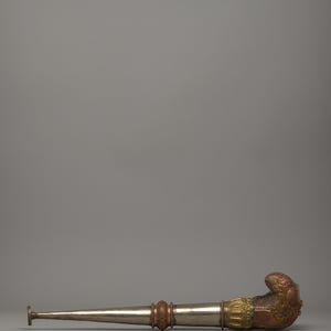 May include: A long, ornate pipe with a silver stem and a detailed, copper-colored bowl. The pipe features decorative bands of gold and reddish-brown metal. The design suggests a ceremonial or collectible item.