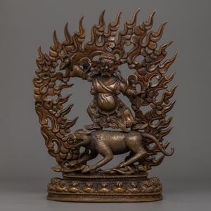 May include: Bronze-colored statue depicting a deity riding a tiger, surrounded by a flame-like halo. The figure has a fierce expression and is adorned with detailed clothing. The base of the statue features intricate patterns.