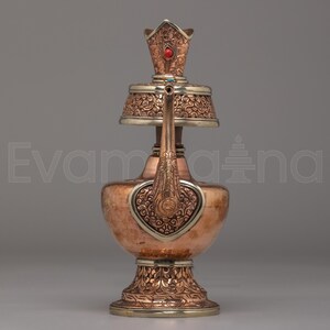 Peut inclure: Une théière en cuivre ornée de détails argentés. Elle présente un motif en forme de cœur, un bec décoratif et un couvercle orné d'une pierre rouge. La base et le sommet sont également décorés de motifs complexes. Le design est détaillé et élégant.