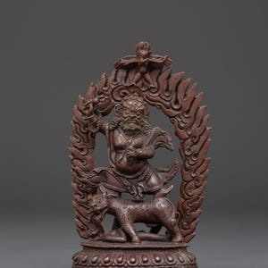 May include: A detailed bronze-colored statue depicting a deity figure with a fierce expression, standing above a tiger-like creature. The figure is surrounded by a flame-like halo, and the statue rests on a detailed base. The overall design suggests a religious or spiritual theme.