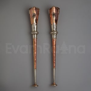 May include: Two decorative copper and silver metal objects with a torch-like design. Each has a flared top with a central oval detail, a silver band, and a long, tapered copper shaft. The bases are silver with a circular foot.