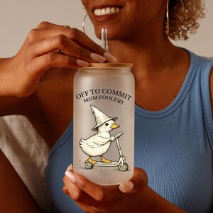 May include: A frosted glass tumbler with a bamboo lid and a straw. The tumbler features a cartoon duck wearing a witch hat and riding a scooter, with the text "OFF TO COMMIT MOM FOOLERY".