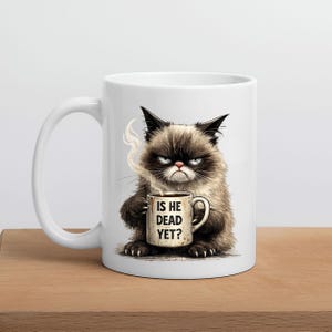 May include: White ceramic mug featuring a grumpy cat illustration holding a coffee cup. The mug has the text "IS HE DEAD YET?" printed on it. The cat is brown and black with an angry expression.