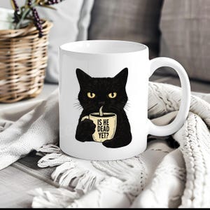 May include: White ceramic mug featuring a black cat with yellow eyes, holding a coffee cup. The cup has the text "IS HE DEAD YET?" in black. The mug has a white handle and is set against a soft, textured background.