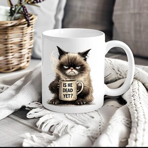May include: White ceramic mug featuring a grumpy cat illustration holding a coffee mug. The coffee mug has the text "IS HE DEAD YET?" in black. The cat is brown and black with a grumpy expression and steam rising from the coffee mug.