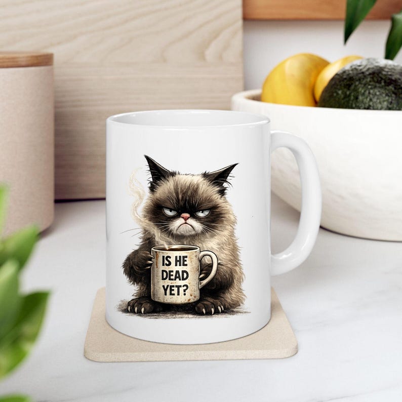 May include: White ceramic mug featuring a grumpy cat illustration holding a coffee cup. The mug has the text "IS HE DEAD YET?" printed on the cup. The cat is brown, black, and white with a displeased expression.