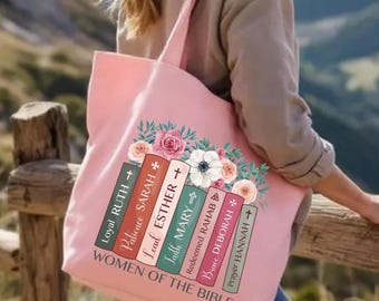 May include: A pink tote bag featuring a floral design and the text "WOMEN OF THE BIBLE." The bag displays a stack of books with names like Ruth, Sarah, and Esther. The bag has a shoulder strap and is held by a person.