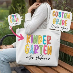 May include: A white tote bag featuring the colorful text KINDERGARTEN in a playful font, with the name Mrs. Williams printed in black script below. The design includes options for FIRST GRADE and CUSTOM GRADE with a custom name placeholder.