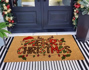 May include: A rectangular doormat with the words "MERRY CHRISTMAS" in a festive design. The text incorporates a Santa hat, reindeer antlers, and holly leaves. The mat has a tan background and is placed on a black and white striped surface.