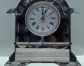 May include: A decorative clock with a clear, faceted arch and base. The clock face is white with black Roman numerals and red hands. The clock's body is a dark, speckled material.