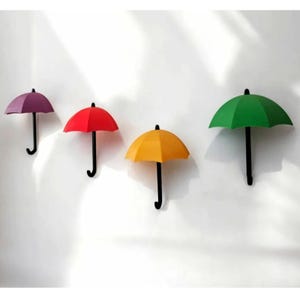 May include: Four colourful umbrella-shaped wall hooks. The hooks are in purple, red, yellow, and green. Each hook has a black handle and is mounted on a white wall. These decorative hooks are ideal for hanging items.