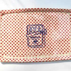 May include: A rectangular ceramic tray with a cream-coloured base featuring a dense pattern of small red polka dots and dark speckles. In the centre, a blue line-art illustration depicts a sardine tin with the text SARDINAS printed on it.