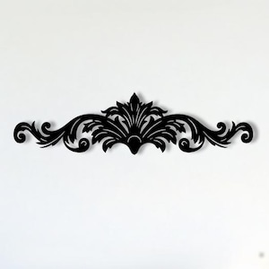 Puede incluir: Decoración de pared negra y ornamentada con un diseño simétrico de hojas arremolinadas y elementos florales. La pieza decorativa está montada en una pared blanca sobre un sofá blanco con cojines azul marino. Una mesa de centro redonda y oscura está frente al sofá.