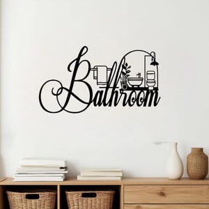 Puede incluir: Arte de pared de baño de metal negro. La palabra "Bathroom" está escrita en una fuente decorativa. El diseño incluye un toallero, una planta, un lavabo, un inodoro y un cabezal de ducha.
