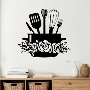 May include: Black metal kitchen wall art featuring a pot with roses and various kitchen utensils. The utensils include a spatula, whisk, egg beater, and fork. The pot is decorated with three roses and leaves.