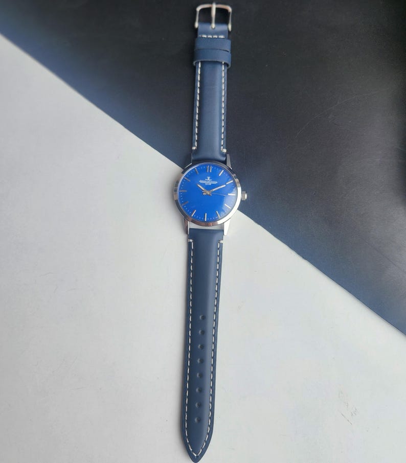May include: A blue wristwatch with a silver case and a matching blue leather strap. The watch face is a vibrant blue with silver hands and markers. The strap is stitched with white thread.