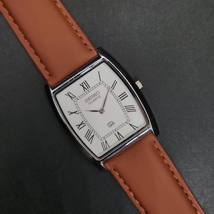 May include: A rectangular Seiko Quartz wristwatch featuring a white dial with black Roman numeral hour markers, a silver-tone case, and a tan leather strap with visible stitching. The dial includes the Seiko Quartz logo and a small SQ symbol.