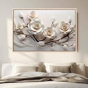 以下が含まれることがあります： 白いバラとつぼみの3Dフローラルデザインが特徴の額入りウォールアート。 アートワークは明るい背景に設定され、ニュートラルな色調の木製フレームが付いています。 画像は、ニュートラルカラーの寝具を備えたベッドの上に表示されます。