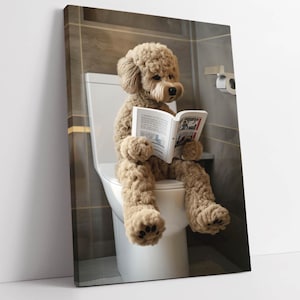 May include: A canvas print depicts a plush dog reading a newspaper while seated on a white toilet. The dog is light brown with a fluffy texture, and the bathroom has gray tile walls. The newspaper is open, displaying printed text and images.