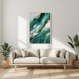 Puede incluir: Impresión artística abstracta con un diseño fluido en tonos verde esmeralda, blanco y dorado. La obra de arte está enmarcada en un marco de madera clara y cuelga sobre un sofá beige con cojines. Dos plantas en macetas flanquean el sofá.