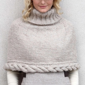 May include: A light beige knitted poncho with a turtleneck collar and a braided cable knit trim along the bottom edge. The poncho is made of a soft, textured yarn and is designed to be worn over the shoulders.