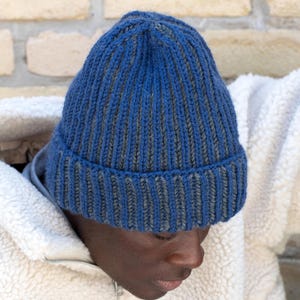 May include: A ribbed knit beanie in shades of blue and gray. The hat is made of a soft, textured yarn and has a folded brim. The beanie is a classic winter accessory, perfect for keeping warm in cold weather.