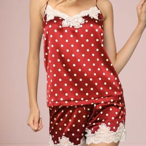 May include: Red satin pajama set with white polka dots. The camisole top has a lace trim along the neckline and spaghetti straps. The matching shorts also have a lace trim along the hemline. The pajama set is a comfortable sleepwear option.