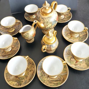 Puede incluir: Un juego de té vintage con acabado dorado, que incluye una tetera, azucarero, jarrita para la leche y varias tazas y platillos. El juego presenta un diseño detallado de paisaje en cada pieza, con detalles dorados. Las tazas y platillos tienen unos 10 cm de diámetro.