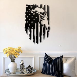 May include: Black metal wall art depicting an American flag with an eagle's head. The flag design features stars and stripes, with the eagle's head on the right side. The art is mounted on a white wall, with decorative items in the foreground.