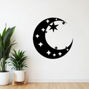 May include: A black crescent moon with various star shapes cut out. The moon is a wall decoration, and the stars are of different sizes and shapes. The wall art is mounted on a white wall, with plants in white pots in the foreground.