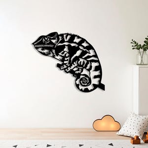 May include: Black and white metal wall art of a chameleon. The chameleon is perched on a branch, with a curled tail. The artwork is a silhouette, with detailed cutouts to show the pattern of the chameleon's skin.