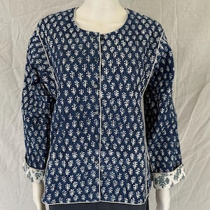 May include: A navy blue jacket with a white floral pattern. The jacket has a round neckline, long sleeves, and a button-up front. The cuffs and collar are trimmed with white fabric. The jacket is made of a quilted material.