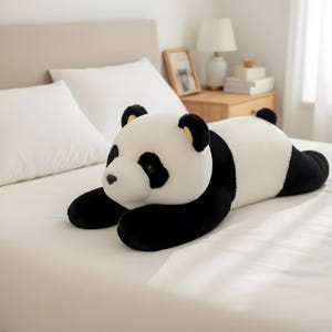 Puede incluir: Un peluche de oso panda en posici&oacute;n horizontal, con un dise&ntilde;o en blanco y negro. El panda tiene patas, orejas y parches oculares negros, con un cuerpo blanco. El juguete est&aacute; sobre una cama blanca.