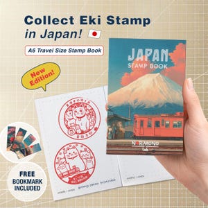 Può includere: Un taccuino di timbri formato viaggio con la scritta "JAPAN STAMP BOOK" e un'illustrazione del Monte Fuji. Il libro è aperto, rivelando disegni di timbri e un adesivo "New Edition". Include un segnalibro gratuito.