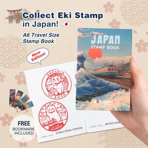 Könnte beinhalten: Ein A6-Reise-Stempelbuch mit einem Cover-Motiv aus Zug, großer Welle und roter Sonne. Das Buch ist geöffnet und zeigt zwei rote Stempelabdrücke mit Katzenmotiven und japanischem Text. Das Cover trägt die Aufschrift Japan Stamp Book.
